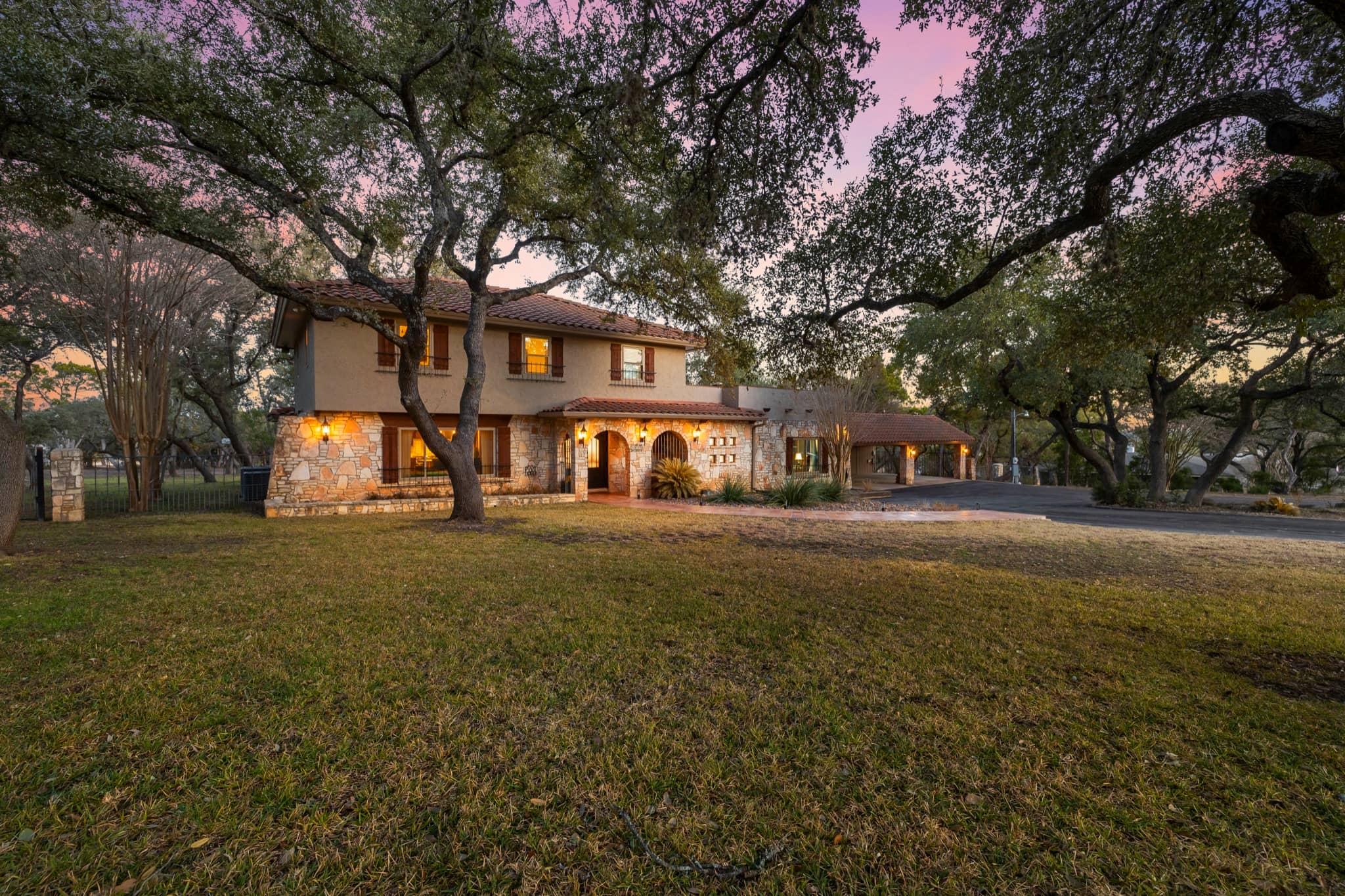 Stone Hill Country home beneath mature oak trees at dusk